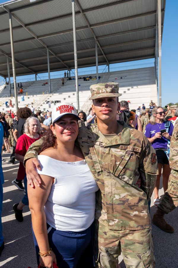A new airman in uniform with his arm around his mother in a crowd after an Air Force graduation